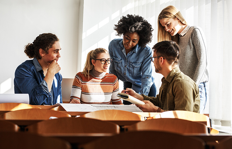 In the university classroom, a group of attentive students gathers, books and notes in hand